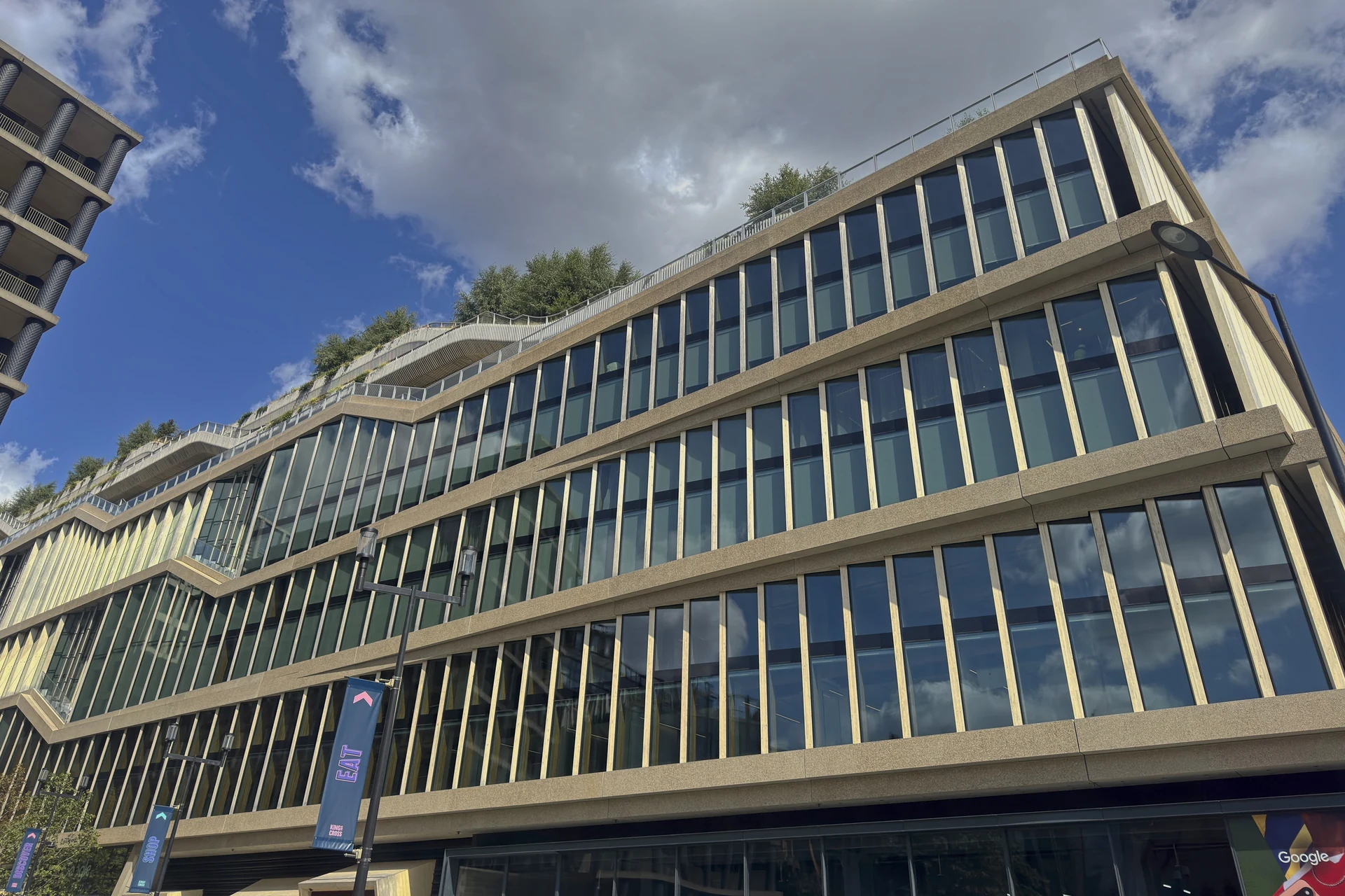 Rows of tall windows on Google’s Platform 37 office, viewed from the street under clouds and blue sky.